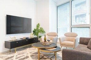 A modern living room with a flat-screen TV, a round coffee table, a sofa, and a large window with blinds.