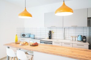 A modern kitchen with white cabinets, a wooden countertop, and two pendant lights.