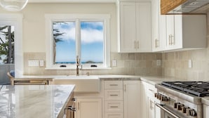 Une cuisine moderne avec des meubles blancs, une grande fenêtre offrant une belle vue et une cuisinière à gaz.