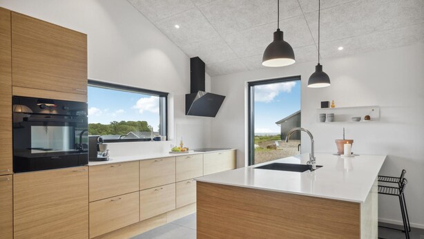 Een moderne keuken met houten kastjes, een ingebouwde oven, een groot raam en hanglampen.