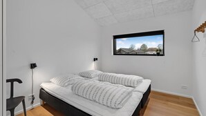 Een slaapkamer met een bed, twee bedlampen, een raam met uitzicht op huizen, en een plafondlamp.