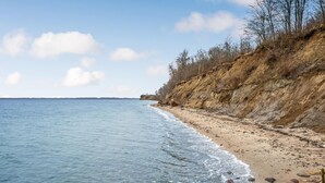 Een strand met helder water, een zandkust en een steile klif met schaarse begroeiing.