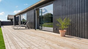 Een modern huis met een houten terras, een glazen deur naar een patio en een potplant.