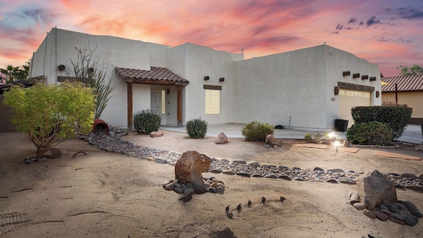 A desert-style house with a white facade, a tiled roof, and a gravel driveway.