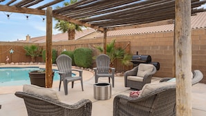 A backyard with a pool, patio furniture, and a grill.