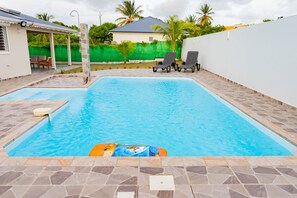 Ein Pool mit gefliestem Sonnendeck, Liegestühlen und einer überdachten Sitzgelegenheit.