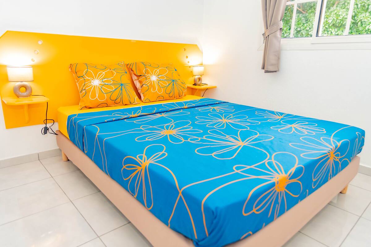 A bright bedroom with a yellow headboard, a blue floral bedspread, and two bedside lamps.