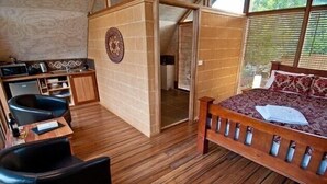 Een kleine kamer met een bed, een bureau en een stoel. Er is een kitchenette met een magnetron en een spoelbak.