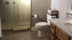 Een badkamer met een douchecabine van glas, een toilet en houten kastjes.