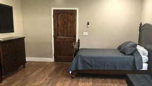 Een slaapkamer met een houten vloer, een bed met een grijze dekbedovertrek, een dressoir en een deur.