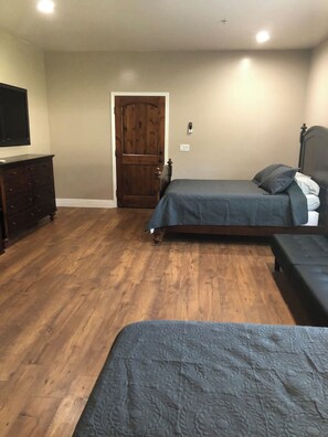 A bedroom with a wooden floor, a bed with a grey bedspread, a dresser, and a door.
