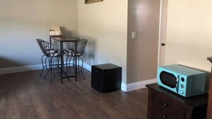 Een kamer met een eettafel en stoelen, een zwarte speaker, een blauwgroene magnetron en een houten dressoir.