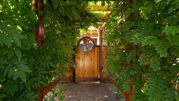 Une tonnelle en bois dotée d’une porte circulaire, entourée d’un feuillage verdoyant et luxuriant.