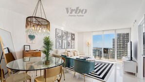 A modern living room with a glass dining table, teal sofas, and a chandelier.