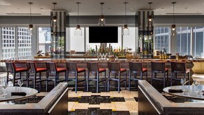 A modern bar area with a long counter, multiple seating options, and a large TV screen.