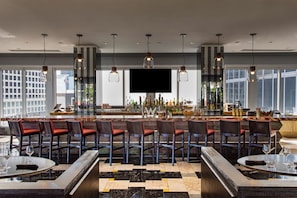 A modern bar area with a long counter, multiple bar stools, and a large TV screen.