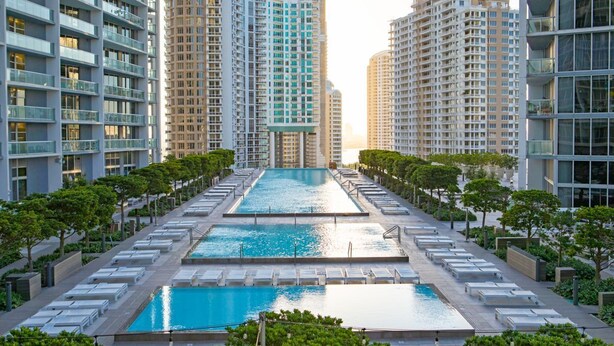 A modern high-rise building with a central swimming pool surrounded by lounge chairs and greenery.