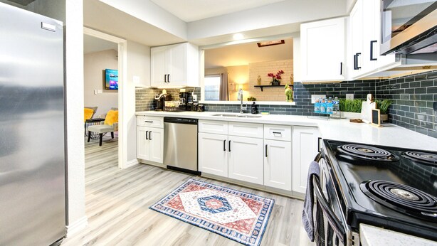 A modern kitchen with white cabinets, a black stove, and a tiled backsplash. - Modern Boho Retreat W/3 Spacious Bedrooms +3Bathrooms +Garage (Houston)