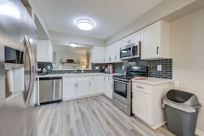 A modern kitchen with white cabinets, stainless steel appliances, and a grey trash bin.