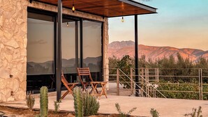 Un edificio moderno con amplios ventanales de vidrio, una pérgola de madera y vistas a las montañas.