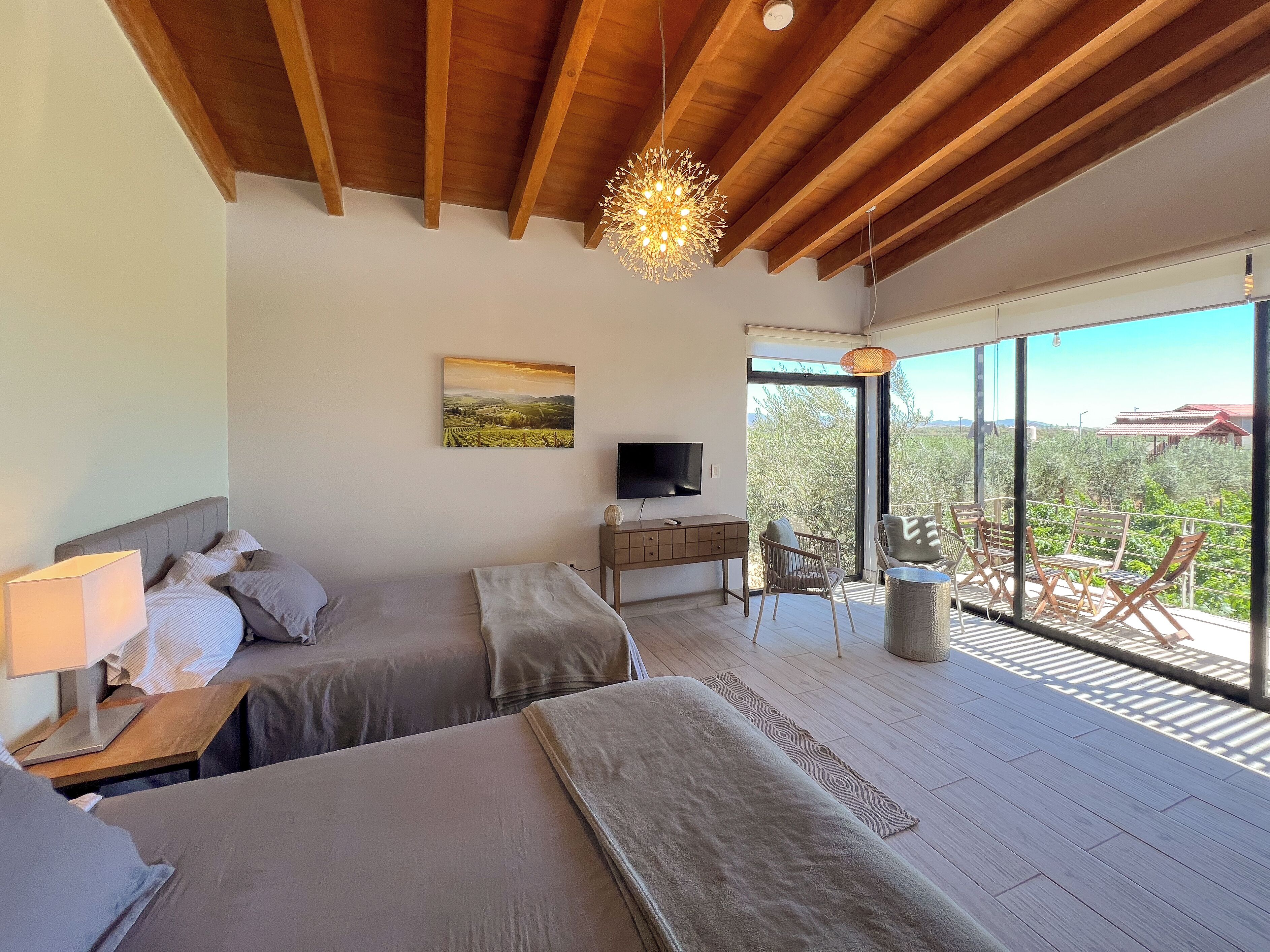 A bedroom with two beds, a desk, a TV, and a balcony with chairs.