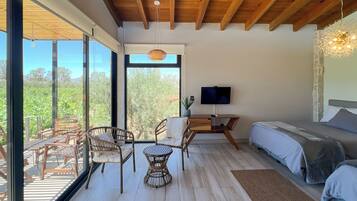 Un dormitorio con cama, televisor y balcón con mobiliario de mimbre y vistas a zonas verdes.