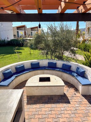 A curved outdoor seating area with blue cushions and a central fire pit. - Valle Soléa (Valle de Guadalupe)