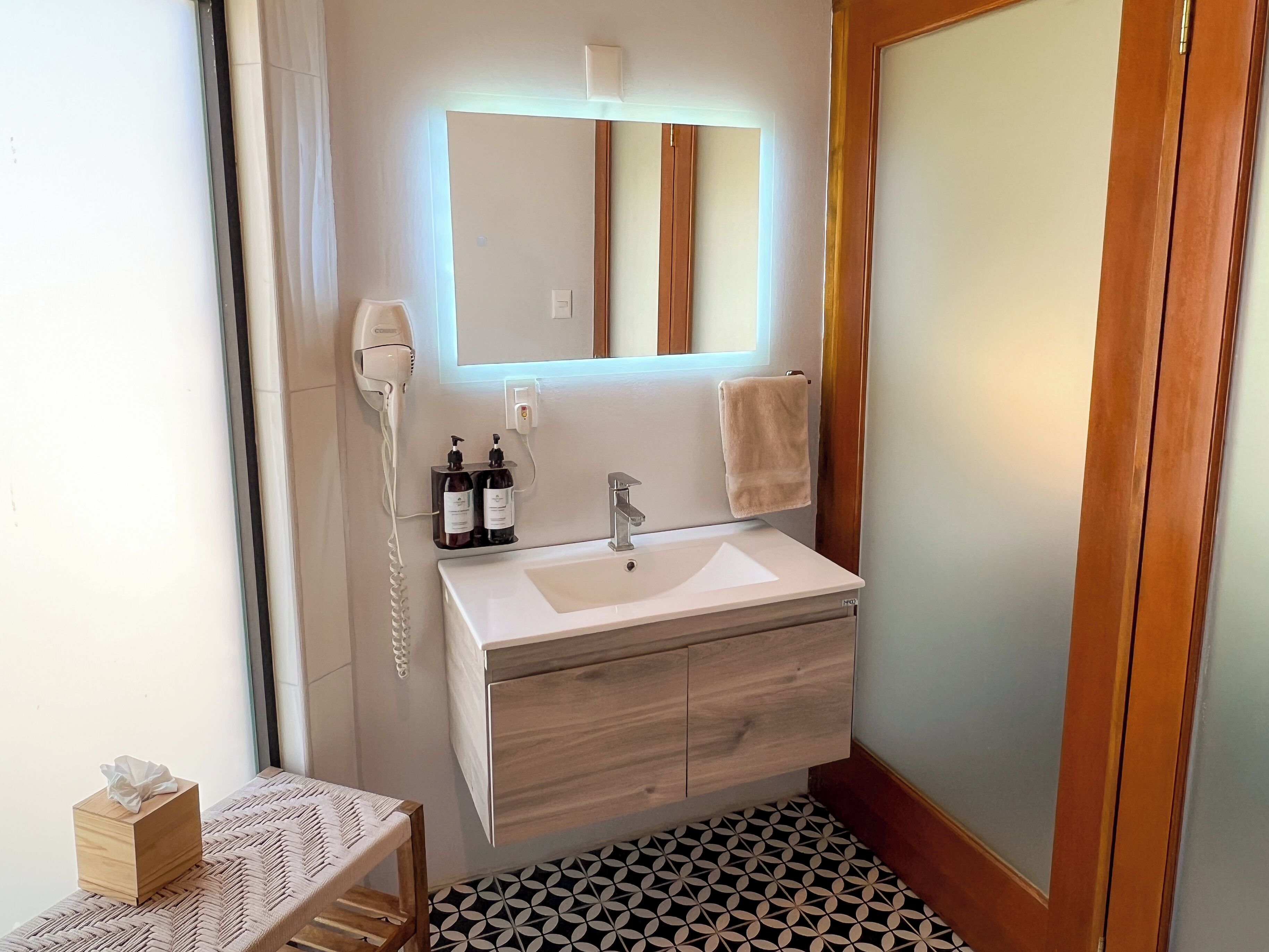 Un baño con lavamanos blanco, tocador de madera, secador de pelo y espejo.