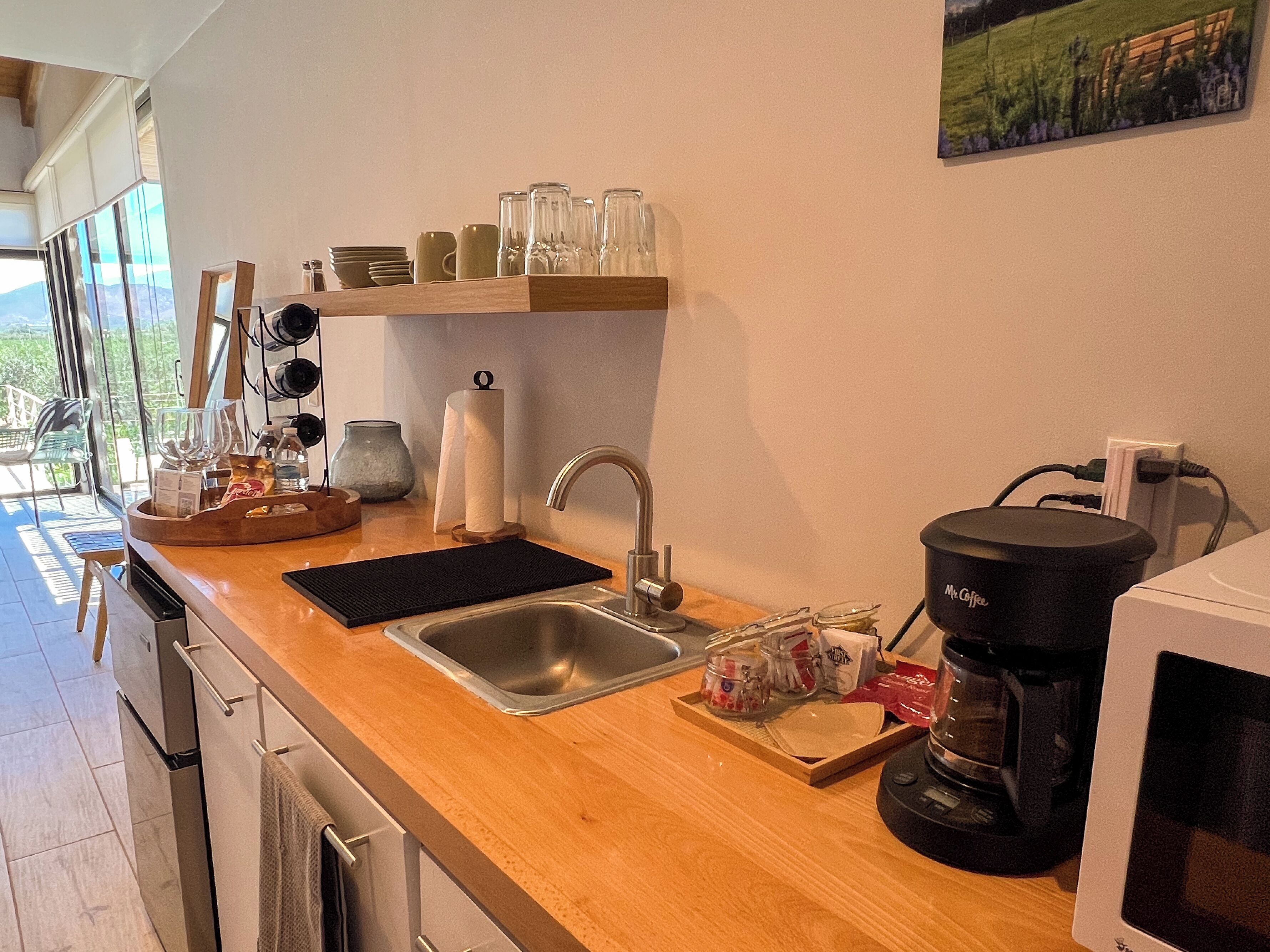 A kitchen with a sink, coffee maker, and shelves with glassware.