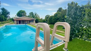 A swimming pool with a beige ladder, a house in the background, and a green hedge. - Patrizio Country House (Labico)