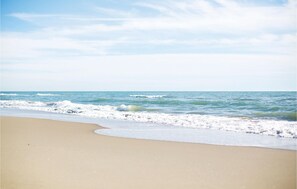 A beach with waves approaching the shore, clear skies, and a sandy beach.