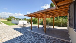 An outdoor patio with stone flooring, wooden pergola, and metal chairs. - Patrizio Country House (Labico)