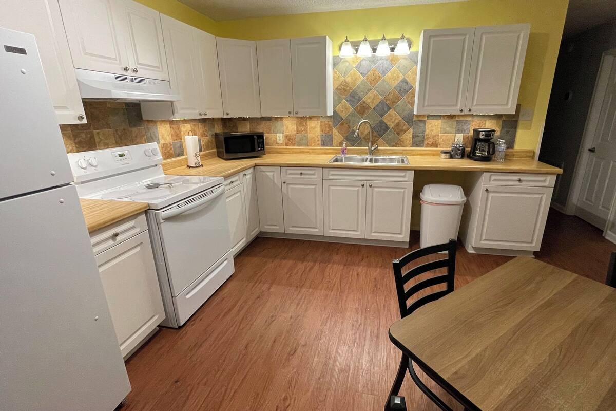 Una cocina compacta con gabinetes blancos, microondas, estufa y pileta.
