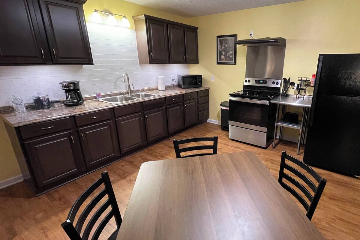 Una cocina compacta con armarios oscuros, una estufa de acero inoxidable, un microondas y un refrigerador.