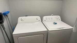 A laundry room with two front-loading washing machines and a blue mop on the left. - O2 Suites Houma (Houma)