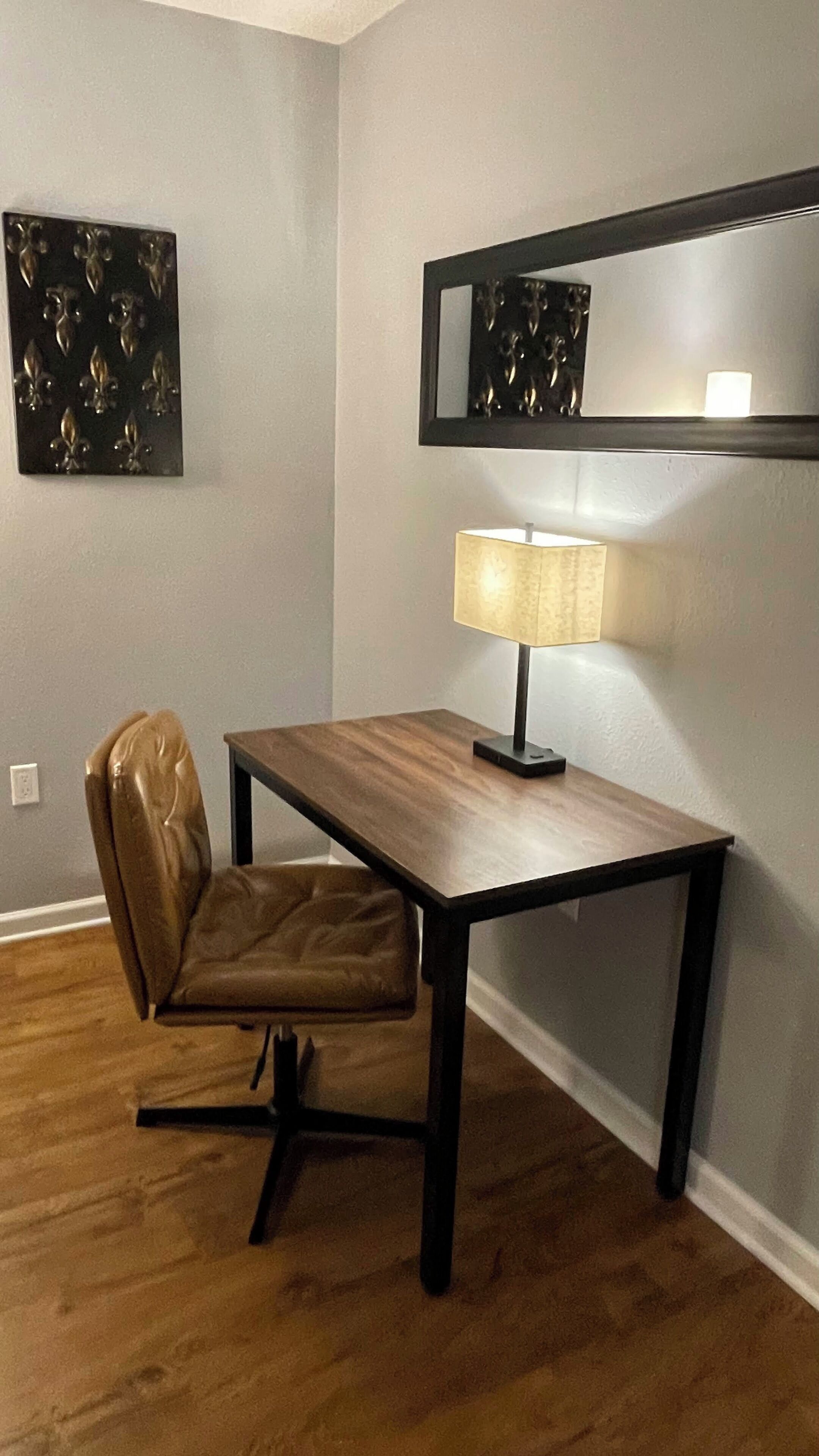 A room with a wooden desk, a leather chair, a lamp, and a wall-mounted mirror.