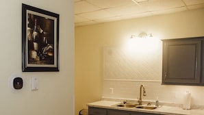 A kitchen with a double sink, dark cabinets, a white tiled backsplash, and a framed artwork on the wall. - O2 Suites Houma (Houma)