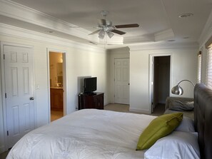 Une chambre avec un grand lit, un ventilateur de plafond, un téléviseur posé sur un meuble et une lampe.