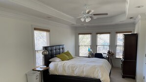A bedroom with a large bed, a ceiling fan, and a desk with a chair.