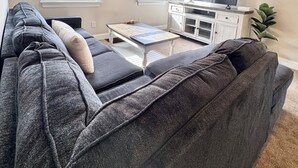 A living room with a dark gray sofa, a coffee table, a flat-screen TV, and a painting of the Mona Lisa. - Downtown Extended Stay ~ Try Purple Mattress Brand - Middlesex County (South Plainfield)