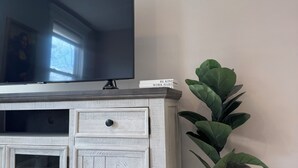 A white wooden cabinet with a flat-screen TV on top, a small plant, and a book titled "BE KIND WORK HARD" on the cabinet. - Downtown Extended Stay ~ Try Purple Mattress Brand - Middlesex County (South Plainfield)