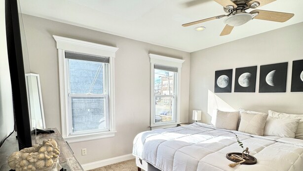A bedroom with a bed, two windows, a ceiling fan, and a wall with moon phase paintings. - Downtown Extended Stay ~ Try Purple Mattress Brand - Middlesex County (South Plainfield)