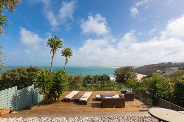 A wooden deck with outdoor furniture overlooking a beach.