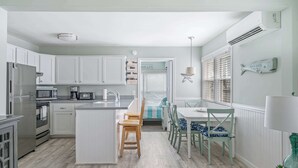 A modern kitchen with white cabinets, stainless steel appliances, and a central island with chairs. - Coastal Condo Close to Beach & Entertainment (Rehoboth Beach)