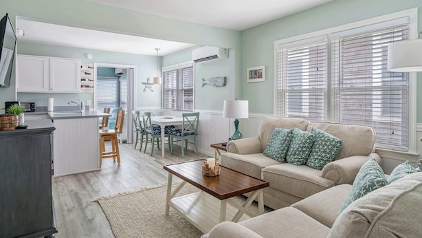 A modern kitchen with white cabinets, a dining area with a table and chairs, and a living room with a sofa and a coffee table. - Coastal Condo Close to Beach & Entertainment (Rehoboth Beach)