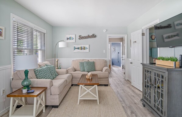 Relax in this stylish living room with a sofa, coffee table, and side table, surrounded by artwork and a large window.