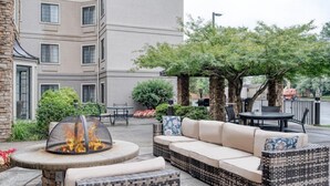 Eine Terrasse mit Feuerstelle, Sitzgelegenheiten im Freien und einem Gebäude im Hintergrund.