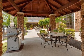 An outdoor patio with a grill, stone pillars, and a round table with chairs.