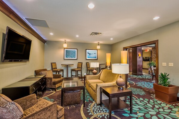 A hotel lobby with a flat-screen TV, comfortable seating, a patterned carpet, and a door leading to another room.