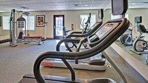Une salle de sport équipée de tapis de course, d’appareils de musculation et d’un banc.